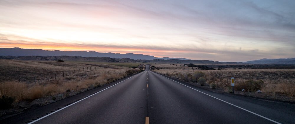 foto de uma estrada rodeada por campos de grama seca sob um ceu durante o por do sol e1681441166606